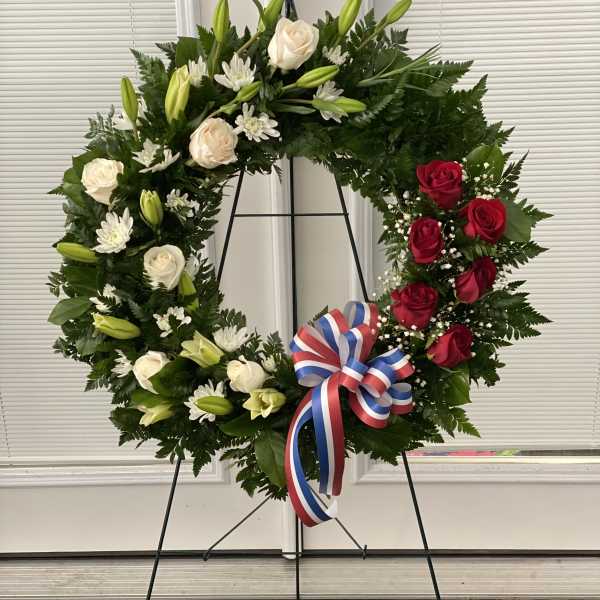 Floral wreath with red and white roses, lilies, and a tricolor ribbon on an easel