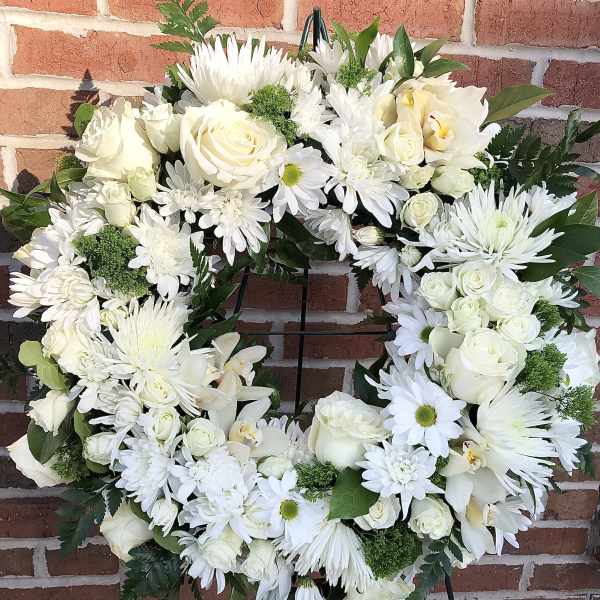 White floral wreath on a black stand with roses and daisies
