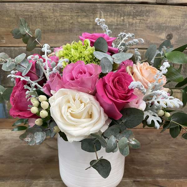 Pink and white roses in a white vase with eucalyptus and a candle nearby