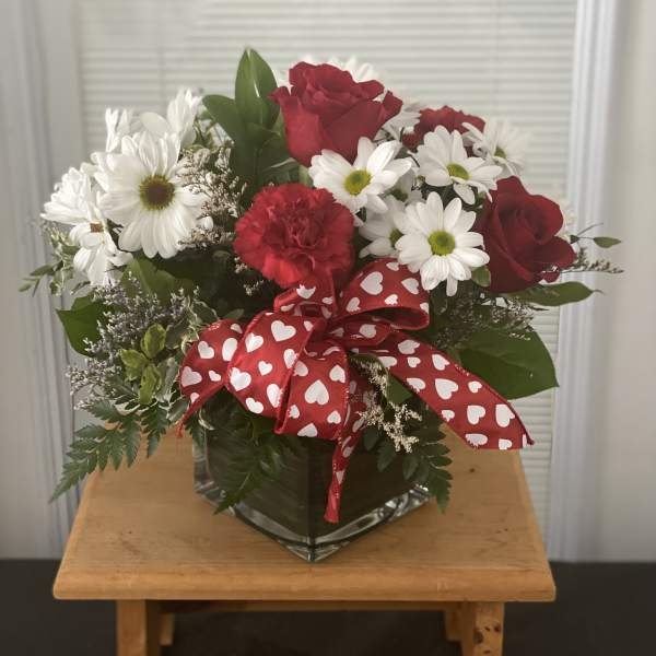 Red roses and white daisies in a glass vase with a heart ribbon
