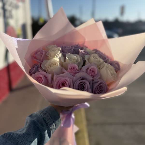 Handheld bouquet of pink, lavender, and white roses wrapped in pale pink paper
