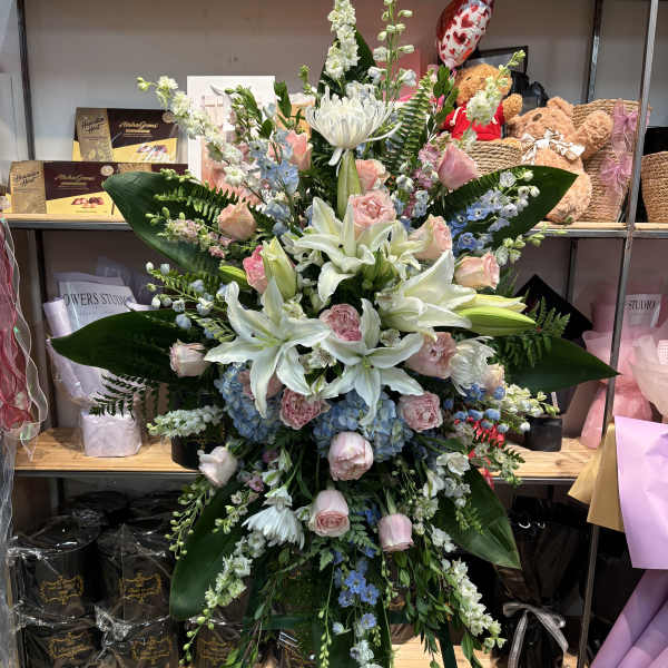 Large standing floral spray with white lilies, pink roses, and blue hydrangeas