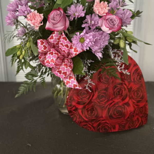 Pink roses and lavender daisies in a glass vase with a heart-pattern ribbon