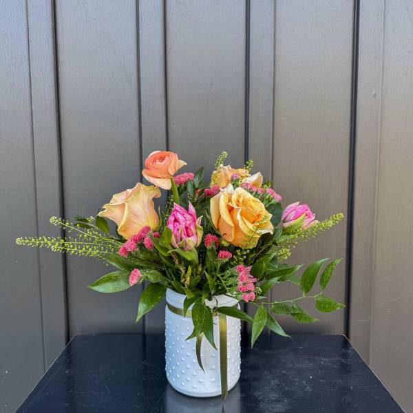 Peach and pink roses with small pink blooms in a white textured vase