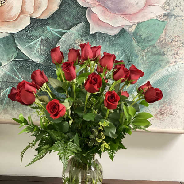 Red roses arranged in a clear glass vase with greenery