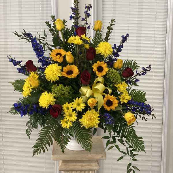 Large mixed flower arrangement in a white vase with yellow, red, and blue blooms