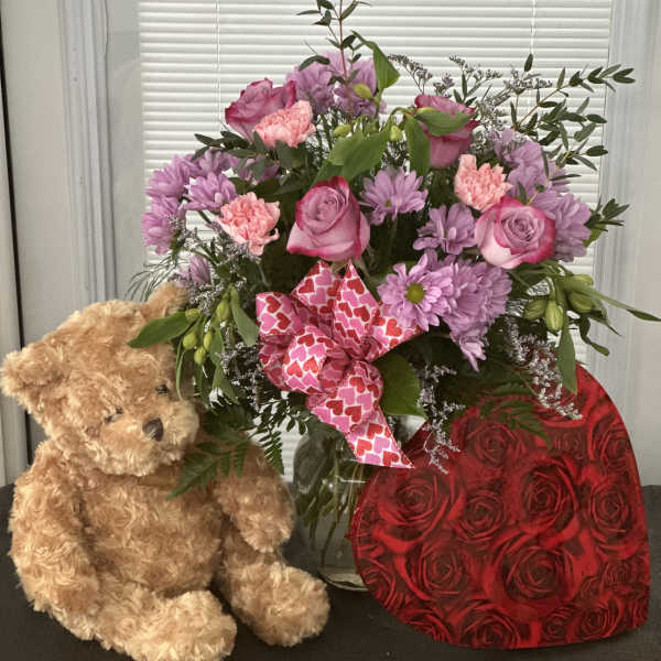Pink and lavender flower arrangement with a teddy bear and heart-patterned ribbon