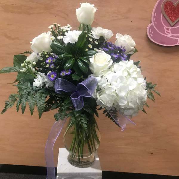 White rose and hydrangea bouquet in a glass vase with purple ribbon