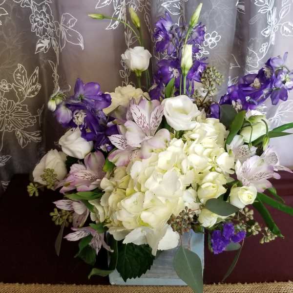 White and purple floral arrangement in a square container
