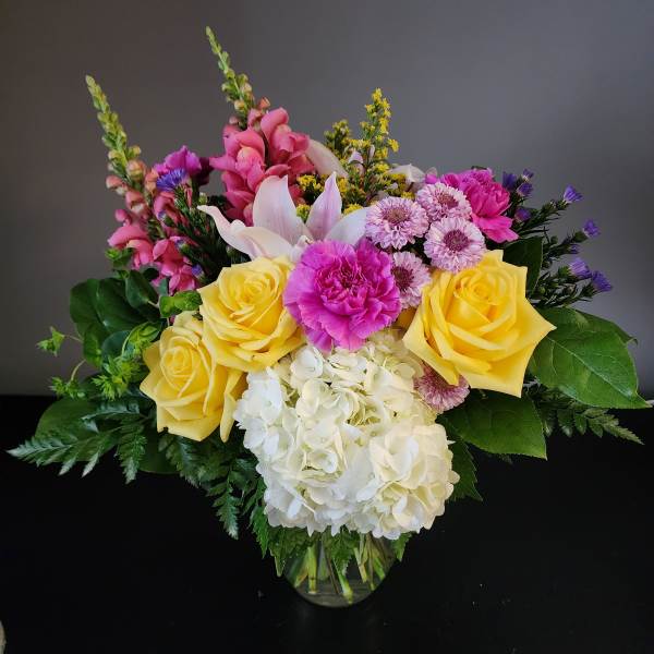 Mixed bouquet of yellow roses, pink blooms, and white hydrangea in a glass vase