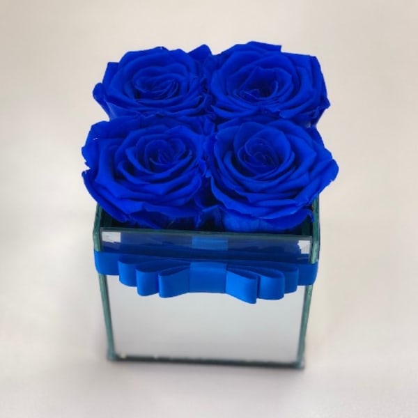 Four blue roses arranged in a square glass vase
