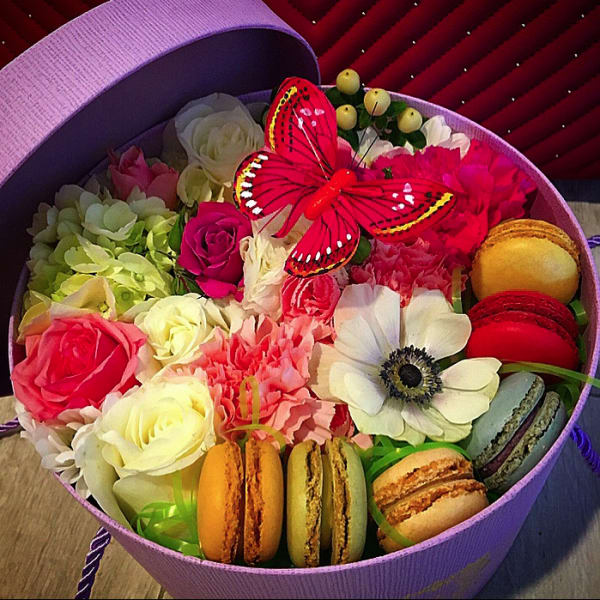 Round box of mixed roses, carnations, anemone, and macarons with a red butterfly topper