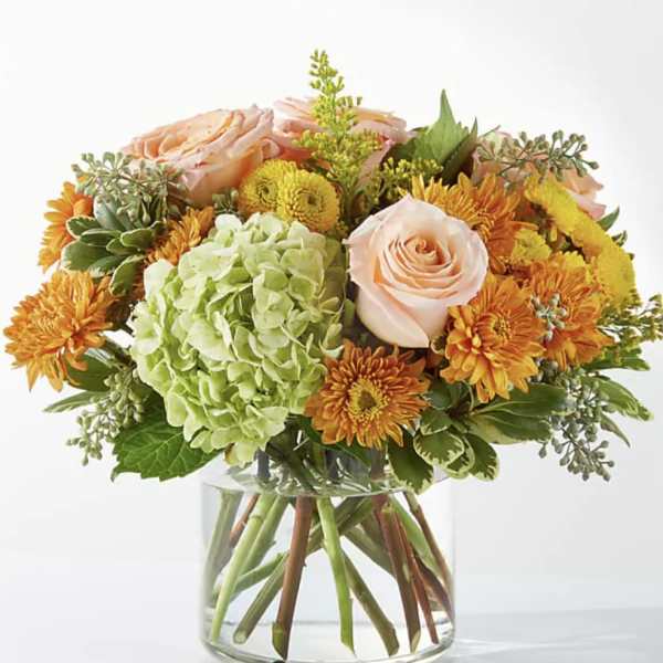 Peach roses and orange mums in a clear glass vase