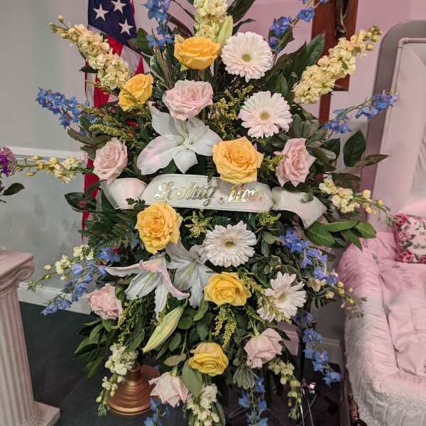 Large funeral spray with roses, lilies, and gerbera daisies on a stand