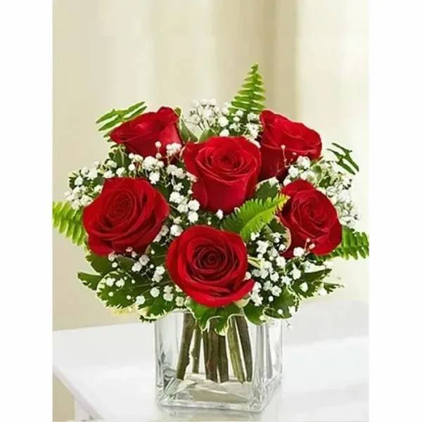 Red roses arranged in a clear square vase with baby's breath.