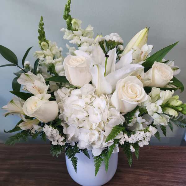 White floral arrangement in a white vase with roses and lilies