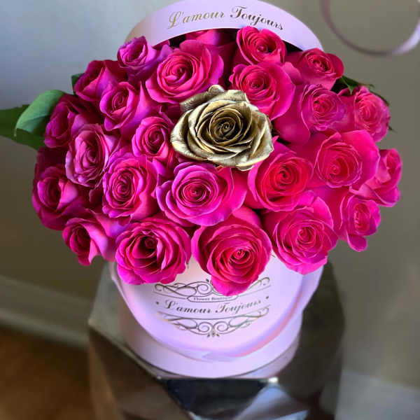 Pink hatbox filled with bright hot pink roses and a single gold rose in the center