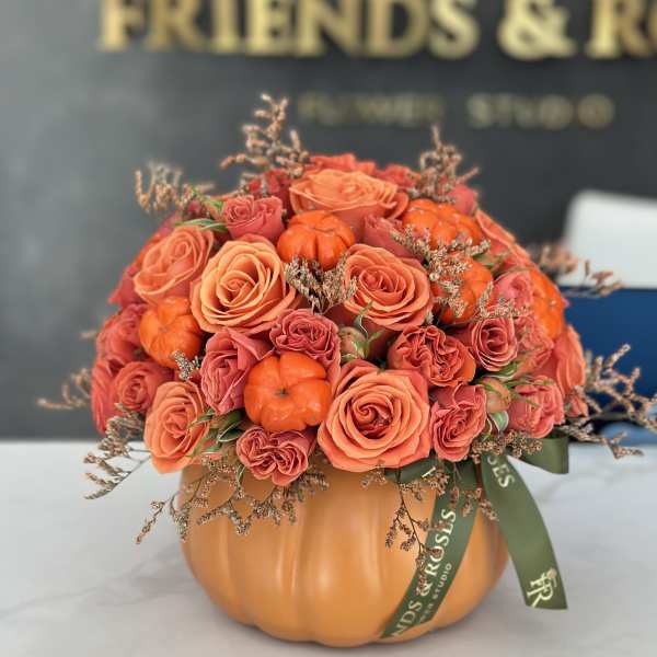 Orange rose arrangement in a pumpkin-shaped container with small orange gourds