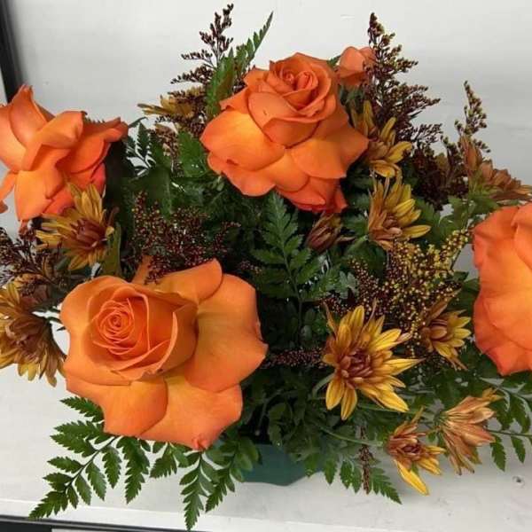 Low arrangement of bright orange roses and golden chrysanthemums in a green container