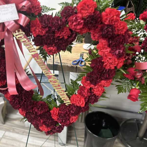 Heart-shaped red and burgundy carnation wreath with pink ribbon