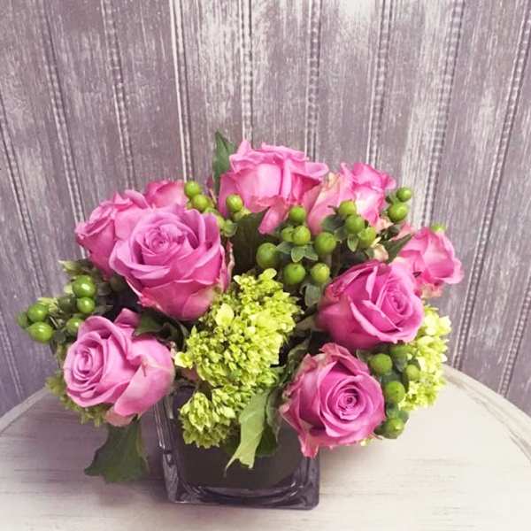 Pink roses arranged in a square glass vase with green accents
