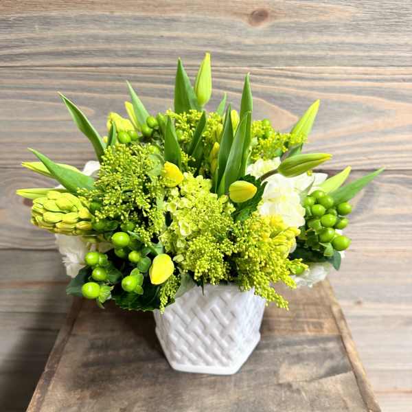Green and yellow floral arrangement in a white woven vase