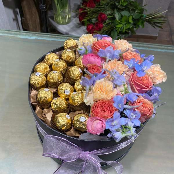 Round gift box with roses, blue flowers, and gold-wrapped chocolates