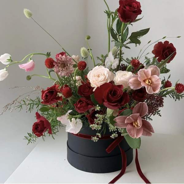 Red and blush floral arrangement in a black hat box with ribbon