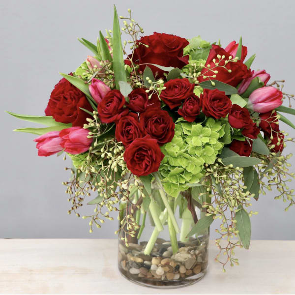Red roses and pink tulips in a glass vase with green hydrangea