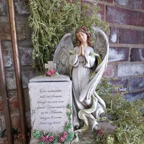 Angel memorial statue beside a stone urn with pink roses