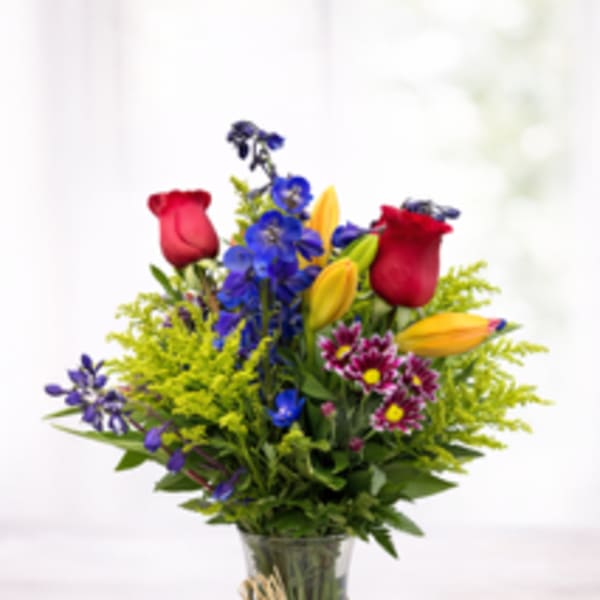 Mixed bouquet of roses, lilies, and blue flowers in a glass vase