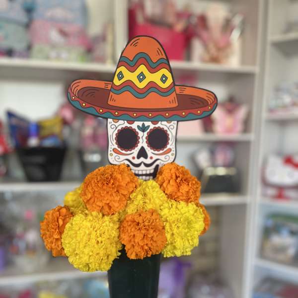 Marigold arrangement with a sugar skull and sombrero topper in a vase
