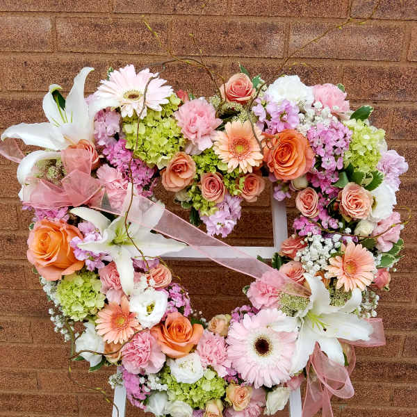 Heart-shaped floral wreath with pink, peach, and white flowers on a stand