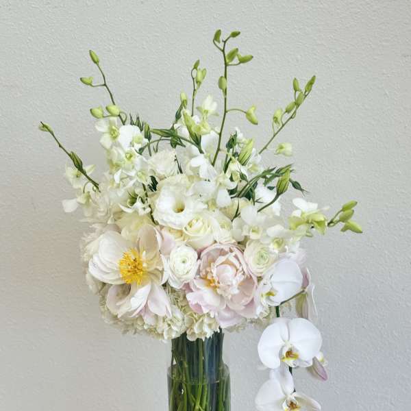 White and blush floral arrangement in a tall glass vase with orchids