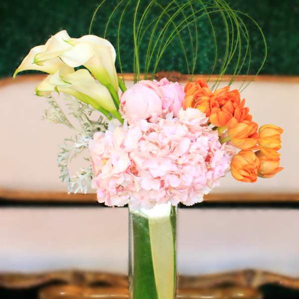 Pink and orange floral arrangement in a tall glass vase