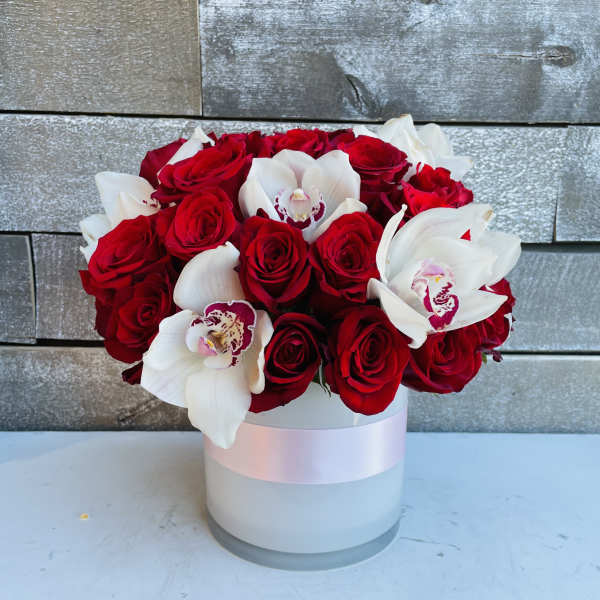 Red roses and white orchids arranged in a white round box