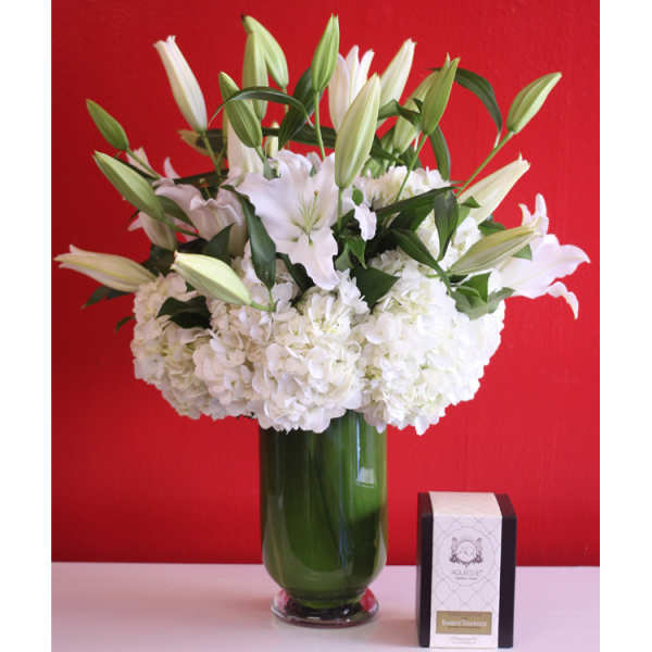 White lilies and hydrangeas in a green glass vase beside a small box