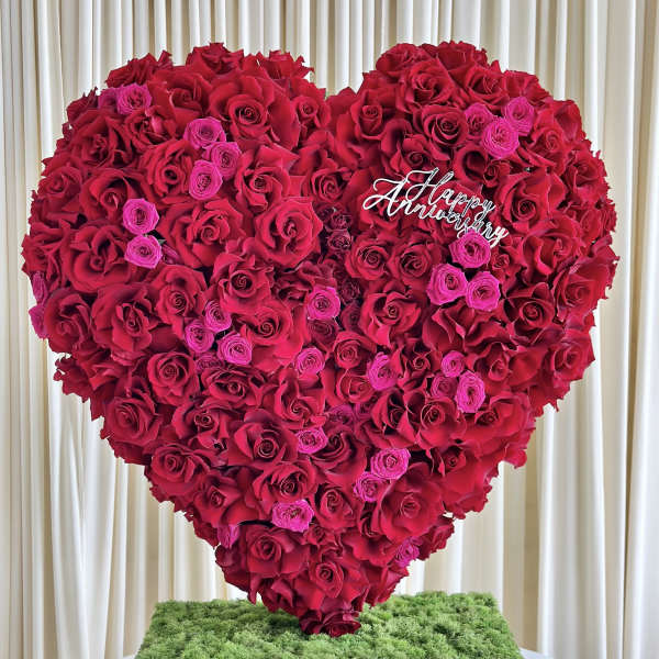 Large heart-shaped arrangement of red and pink roses on moss-topped gold base with Happy Anniversary sign
