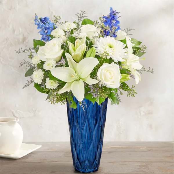 White lilies and roses in a blue glass vase with blue accents