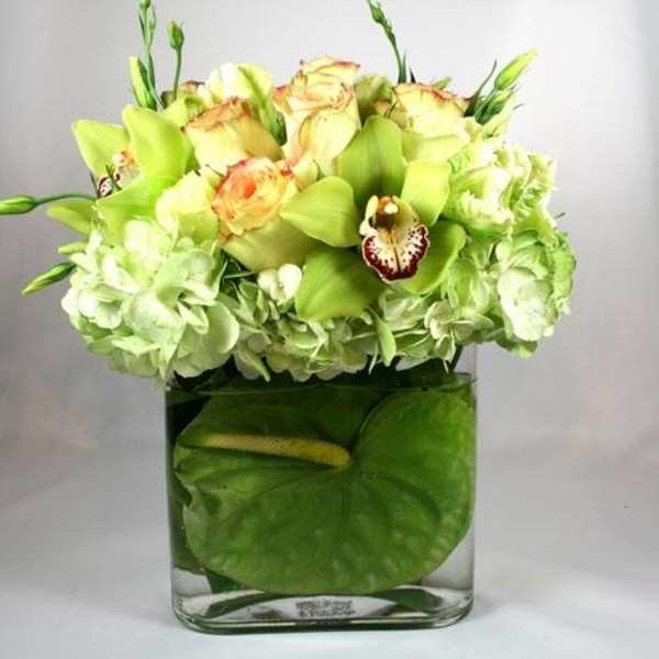 Green and white floral arrangement in a square glass vase