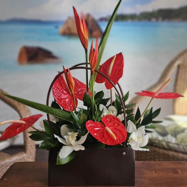 Tropical floral arrangement with red anthuriums and white orchids in a dark container