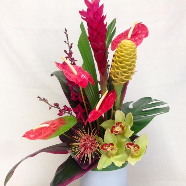 Tropical flower arrangement in a white vase with red anthuriums and yellow orchids