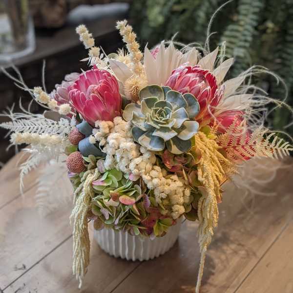 Pink protea and succulents arranged in a white vase