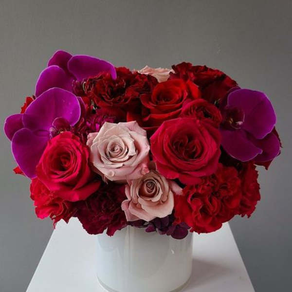 Red and pink roses with purple orchids in a white vase