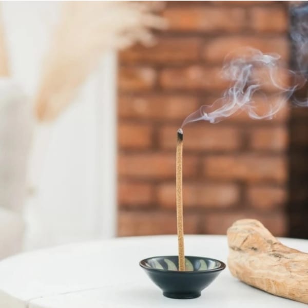 Lit incense stick in a small bowl with smoke rising