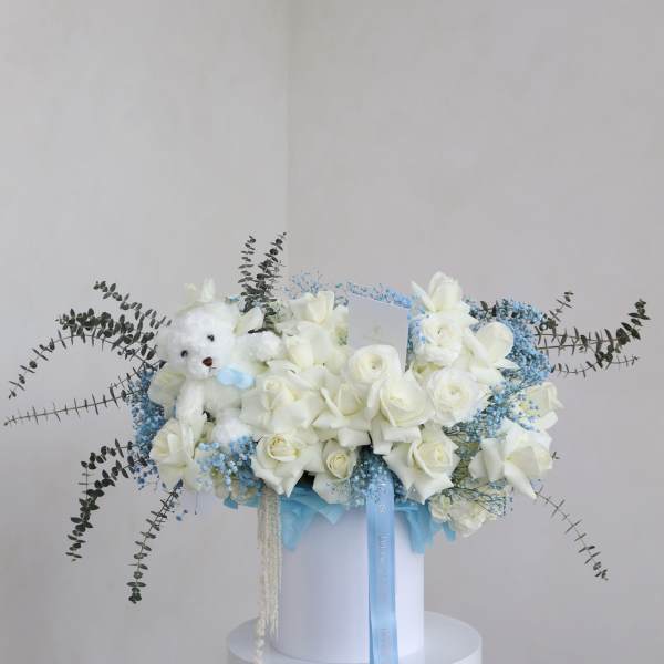 White rose bouquet with a teddy bear and blue ribbon in a white box