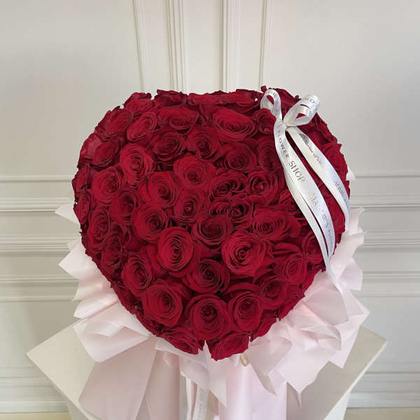 Heart-shaped bouquet of red roses with pale pink wrapping and white ribbon