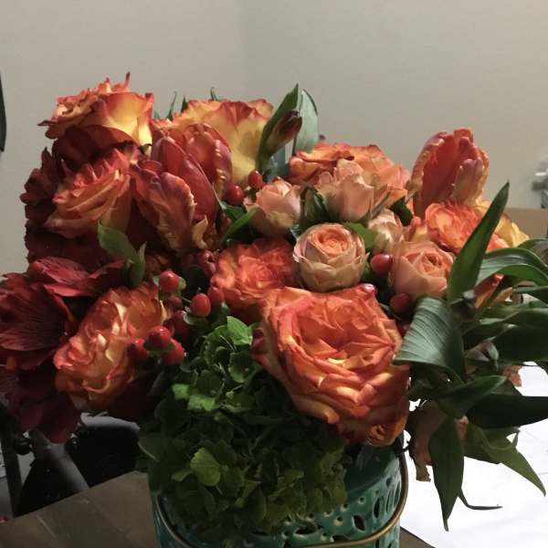 Orange and peach roses arranged in a teal ceramic vase