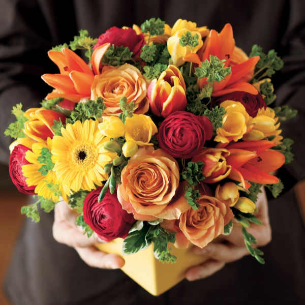 Mixed bouquet of orange, yellow, and red flowers in a yellow box