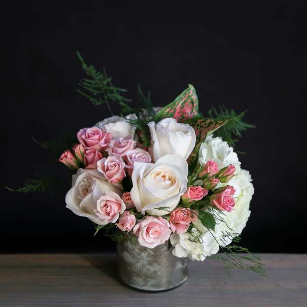 Compact arrangement of white and pink roses with hydrangeas in a silver vase